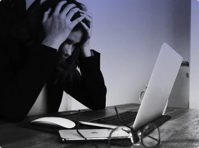 A person sitting at a desk with a closed laptop, head in both hands