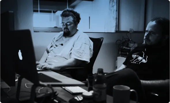 Two developers working at desktop machines in a dimly lit room