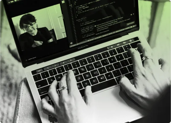 Hands typing on a laptop showing a code editor beside a video call