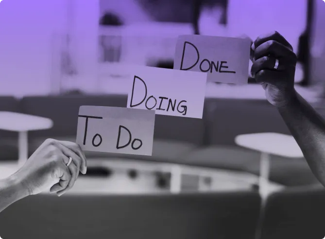 Two people holding up handwritten cards reading To Do, Doing and Done