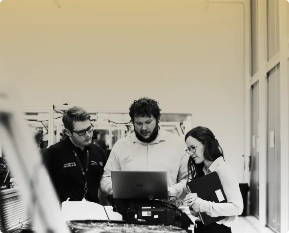 Three colleagues looking together at a laptop beside industrial equipment