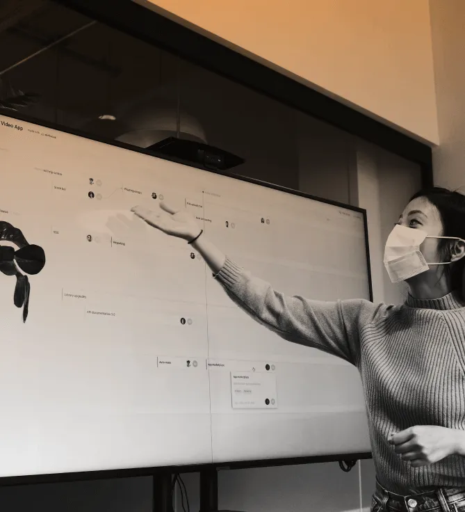 A person pointing at a wall-mounted screen showing a project board