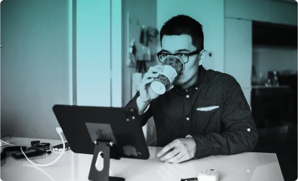 A person drinking from a takeaway cup at a desk with a tablet on a stand