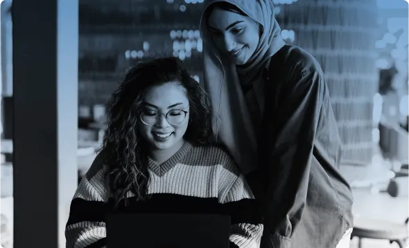 Two colleagues looking at the same screen, one leaning over the other shoulder